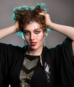 Blue shadow. Leah Bell in a stylised portrait with hands in hair, lit with blue backlight.