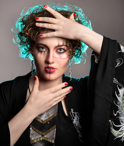 Framed in light. Leah Bell in a stylised portrait framing the face with hands, softly backlit.