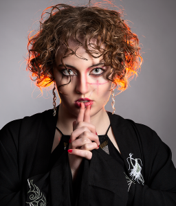 Hush. Leah Bell in a stylised portrait with a finger to the lips, red backlighting through the hair.