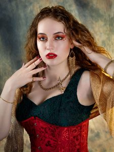 Gilded stillness. Leah Bell in an elegant pose against a smoky gold background, wearing a black, red, and gold outfit.