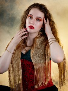 Ember and echo. Leah Bell in an elegant pose against a smoky gold background, wearing a black, red, and gold outfit.