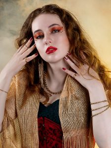 Stillness, held in light. Leah Bell in an elegant pose against a smoky gold background, wearing a black, red, and gold outfit.